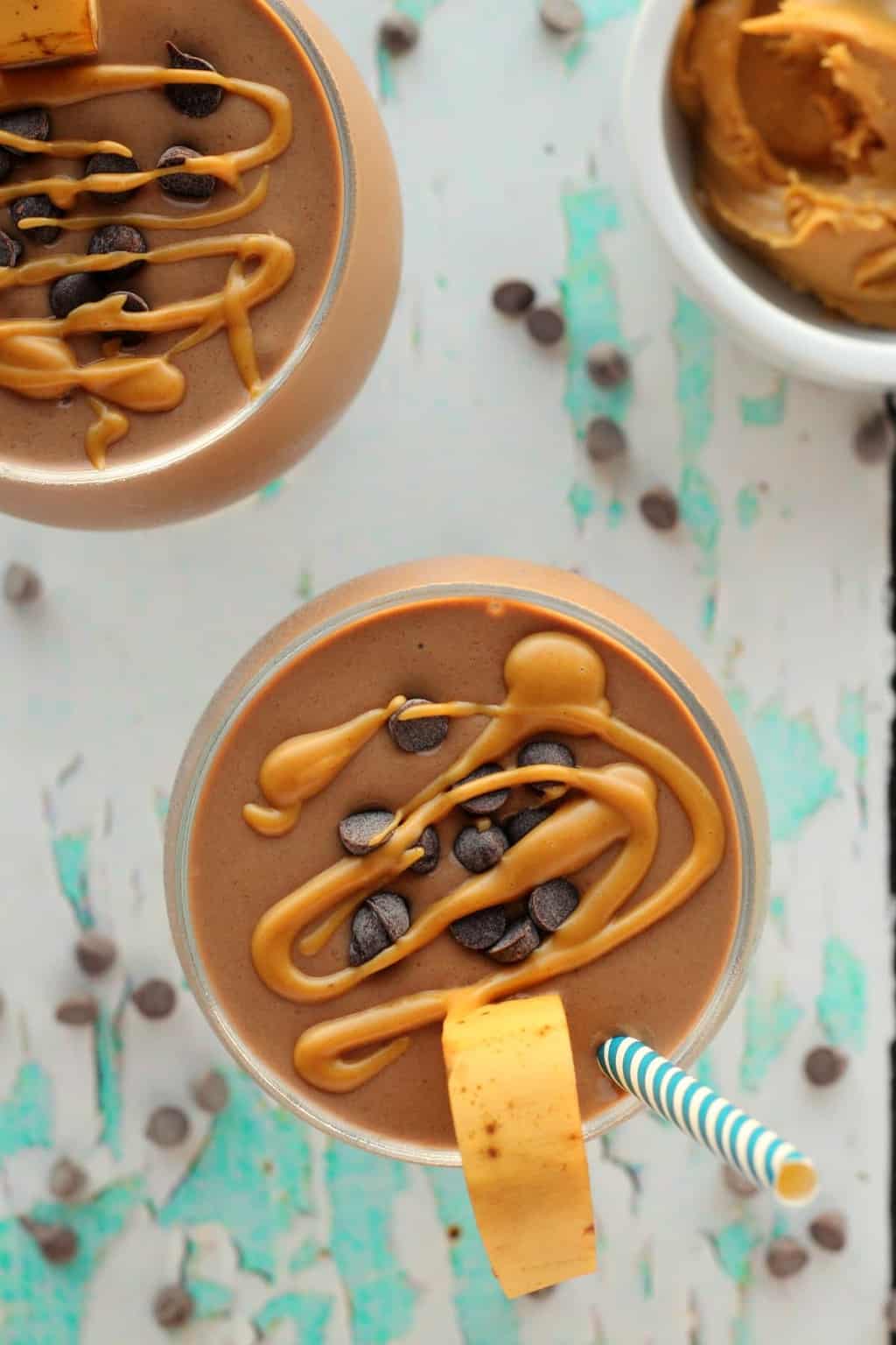 Chocolate peanut butter smoothie topped with chocolate chips and drizzled peanut butter in glasses.