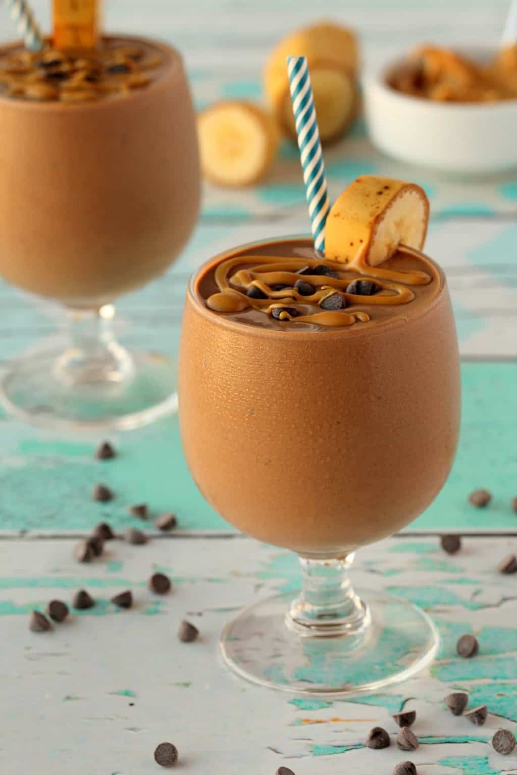 Chocolate peanut butter smoothie in a glass with a blue and white striped straw.
