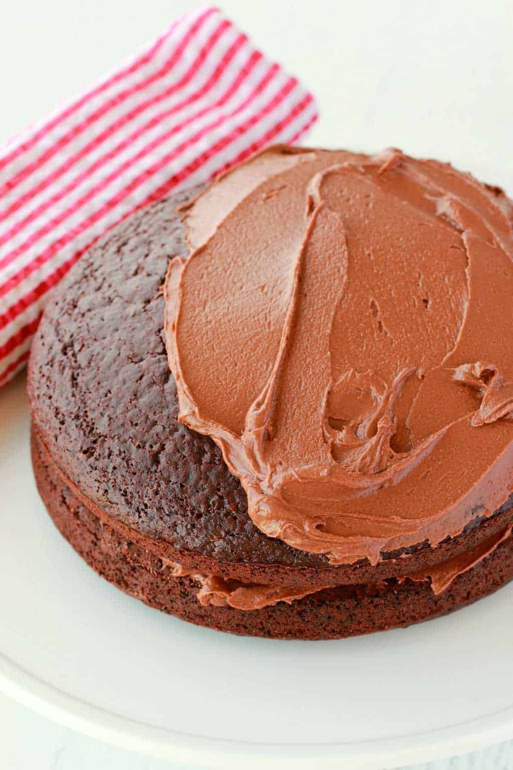 Vegan chocolate cake partially frosted with chocolate frosting.