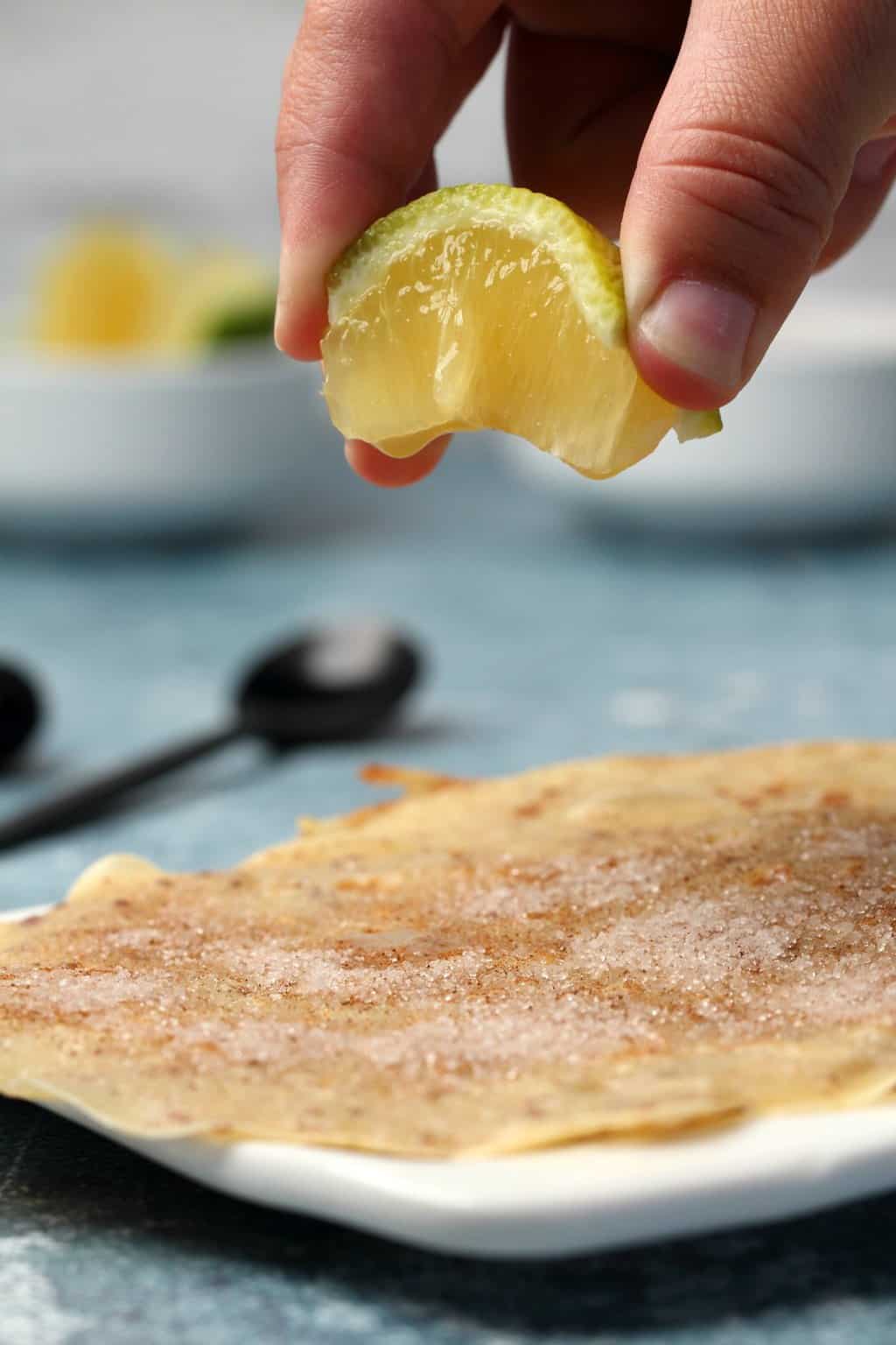 A wedge of lemon being squeezed onto a cinnamon sugar covered vegan crepe. 
