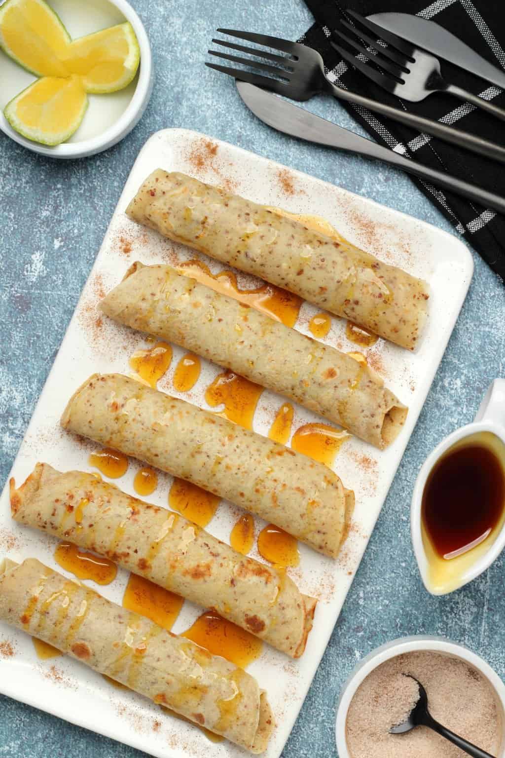 Vegan crepes rolled up on a white plate and drizzled with syrup. 