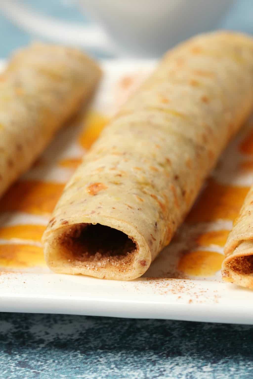 Vegan crepes rolled up and drizzled with syrup on a white plate. 