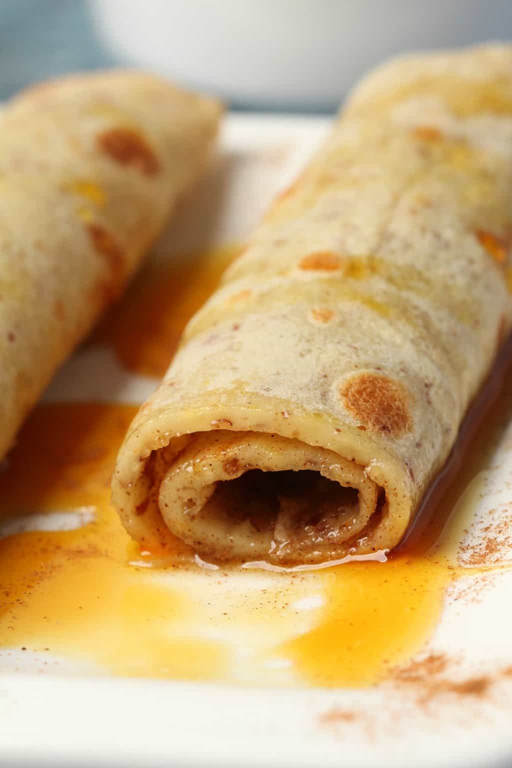 Vegan crepes rolled up on a white plate and drizzled with syrup