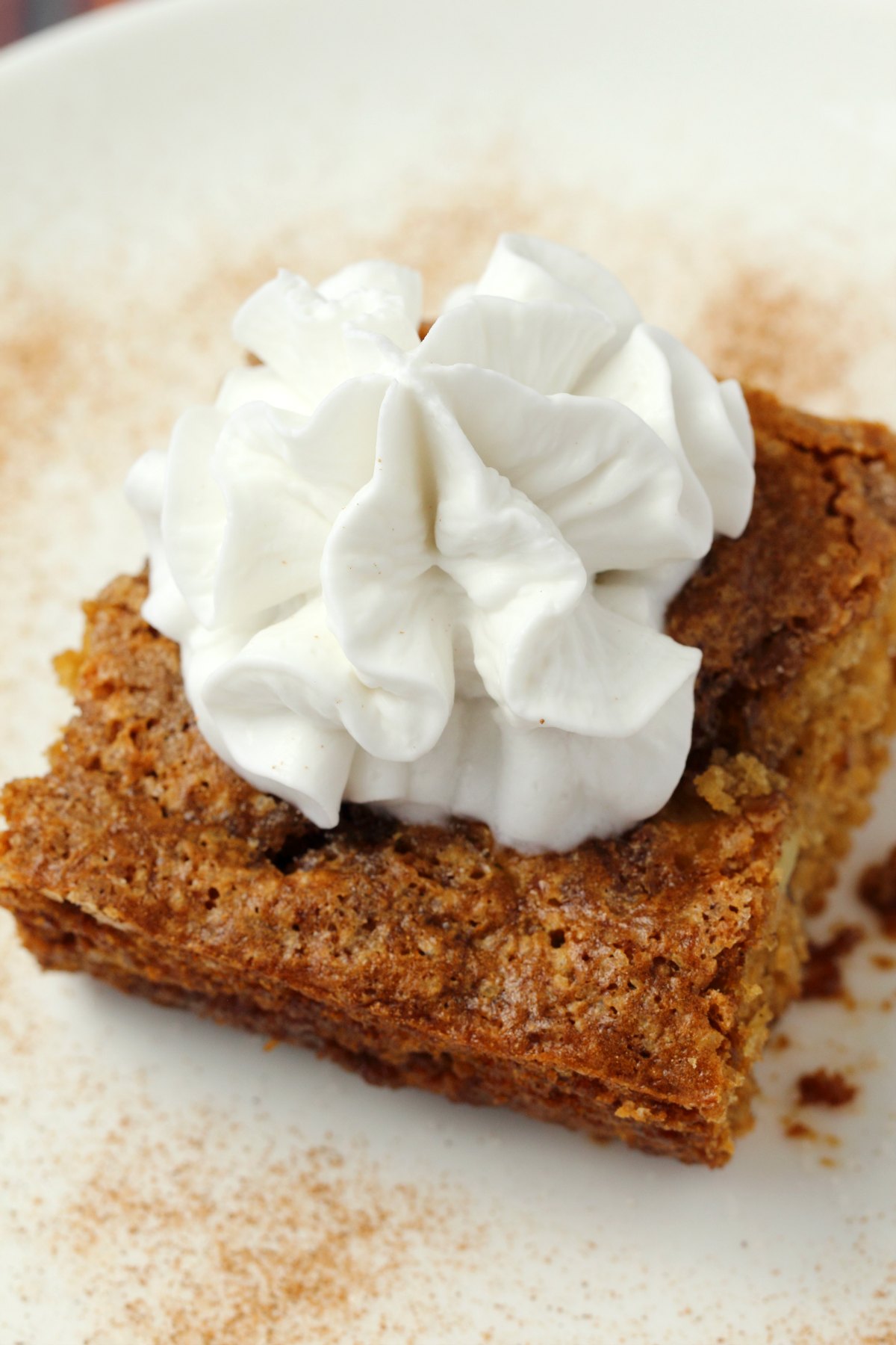 Slice of apple cake topped with vegan whipped cream on a white plate. 