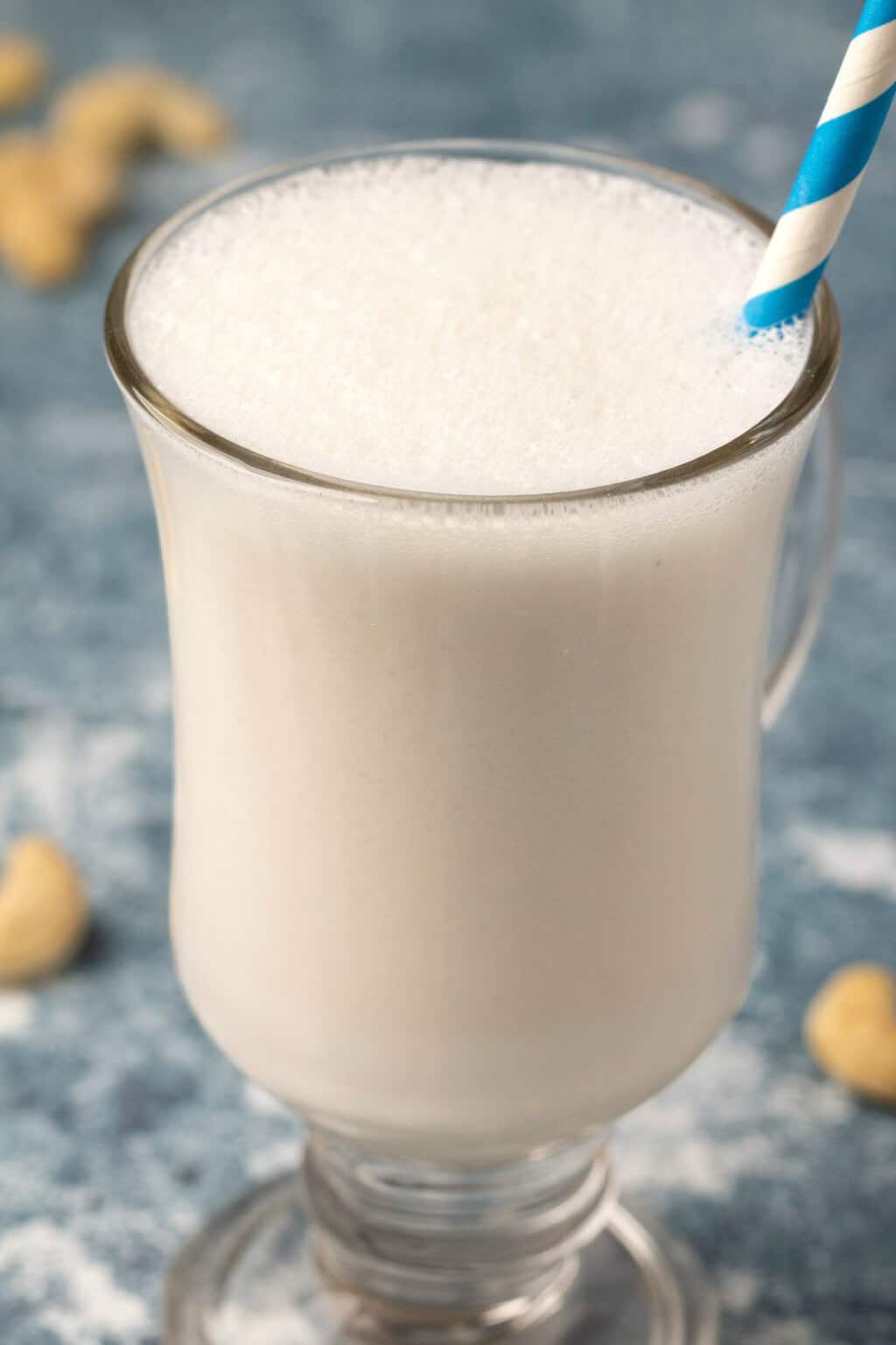 Cashew milk in a glass with a blue and white straw. 