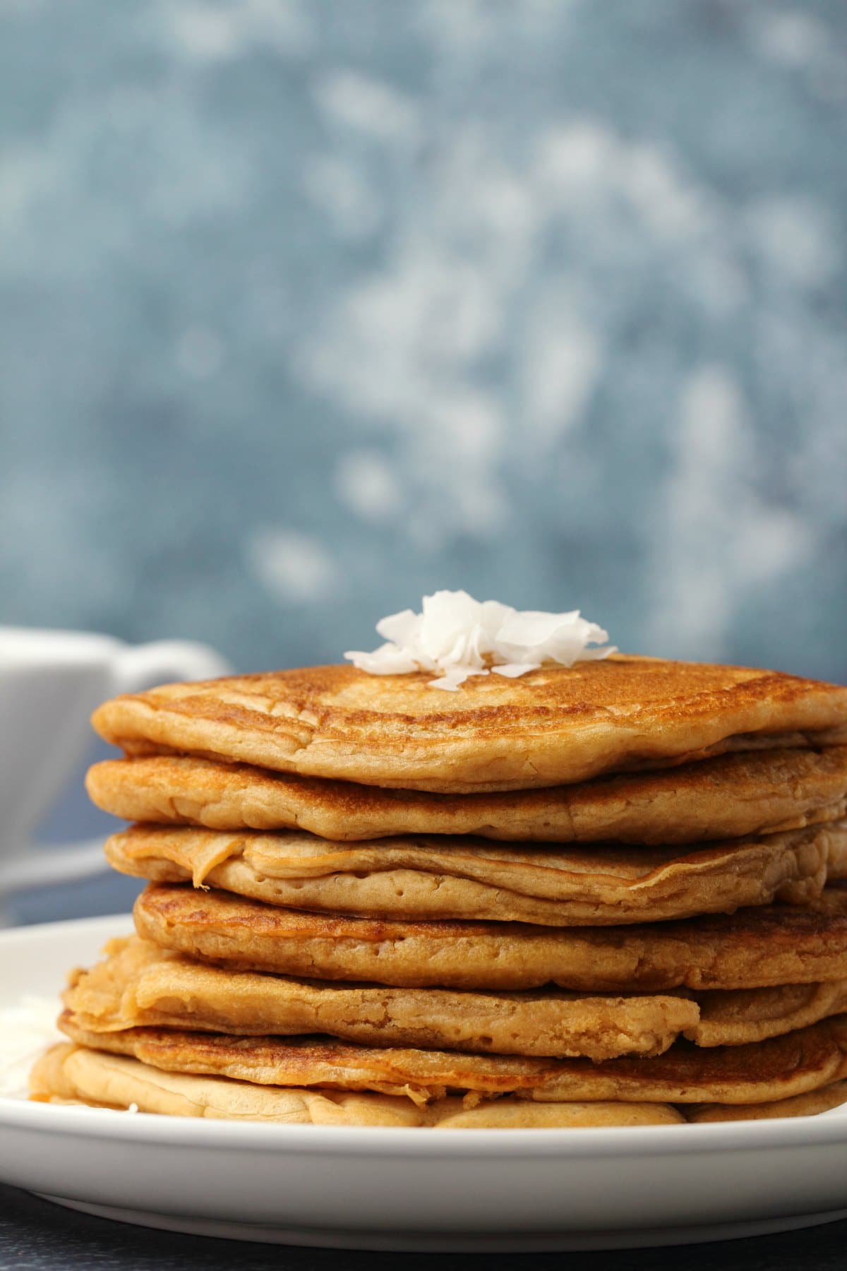 Vegan coconut pancakes topped with coconut flakes and stacked up on a white plate. 