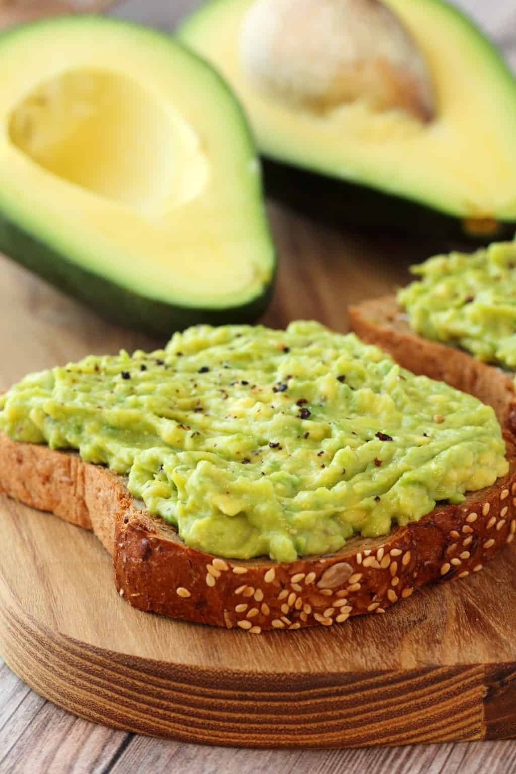 Avocado toast topped with black pepper. Avocado halves in the background. 