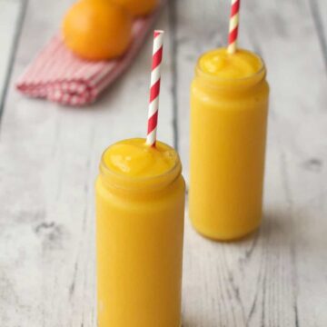 Mango orange smoothie in glasses with striped straws.