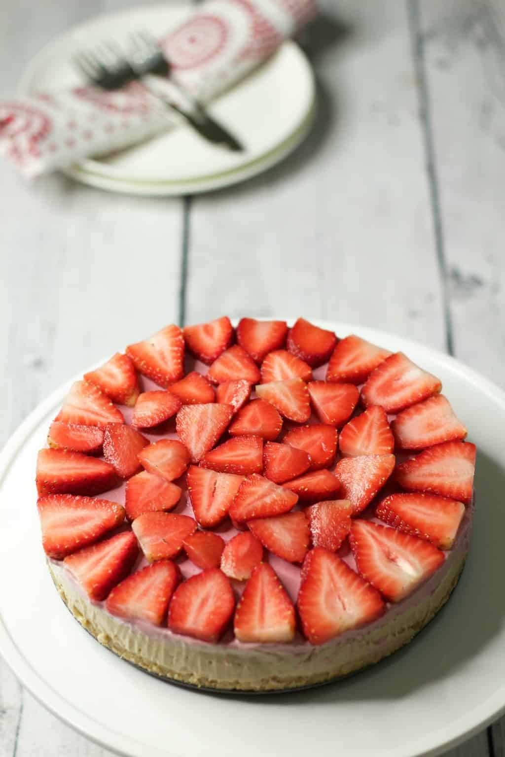 Raw strawberry cheesecake on a white cake stand. 