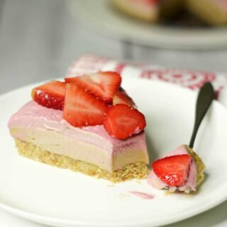 Slice of strawberry cheesecake on a white plate with a cake fork.