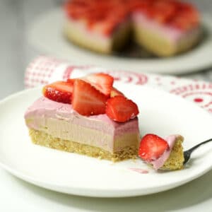 Slice of raw strawberry cheesecake on a white plate with a cake fork.