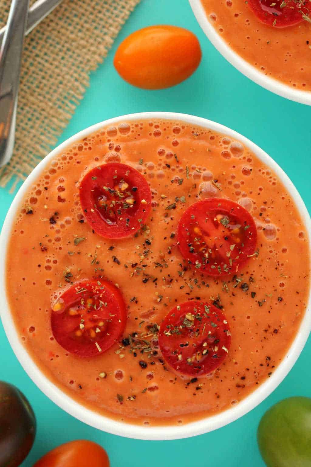 Raw tomato soup topped with sliced cherry tomatoes in a white bowl.