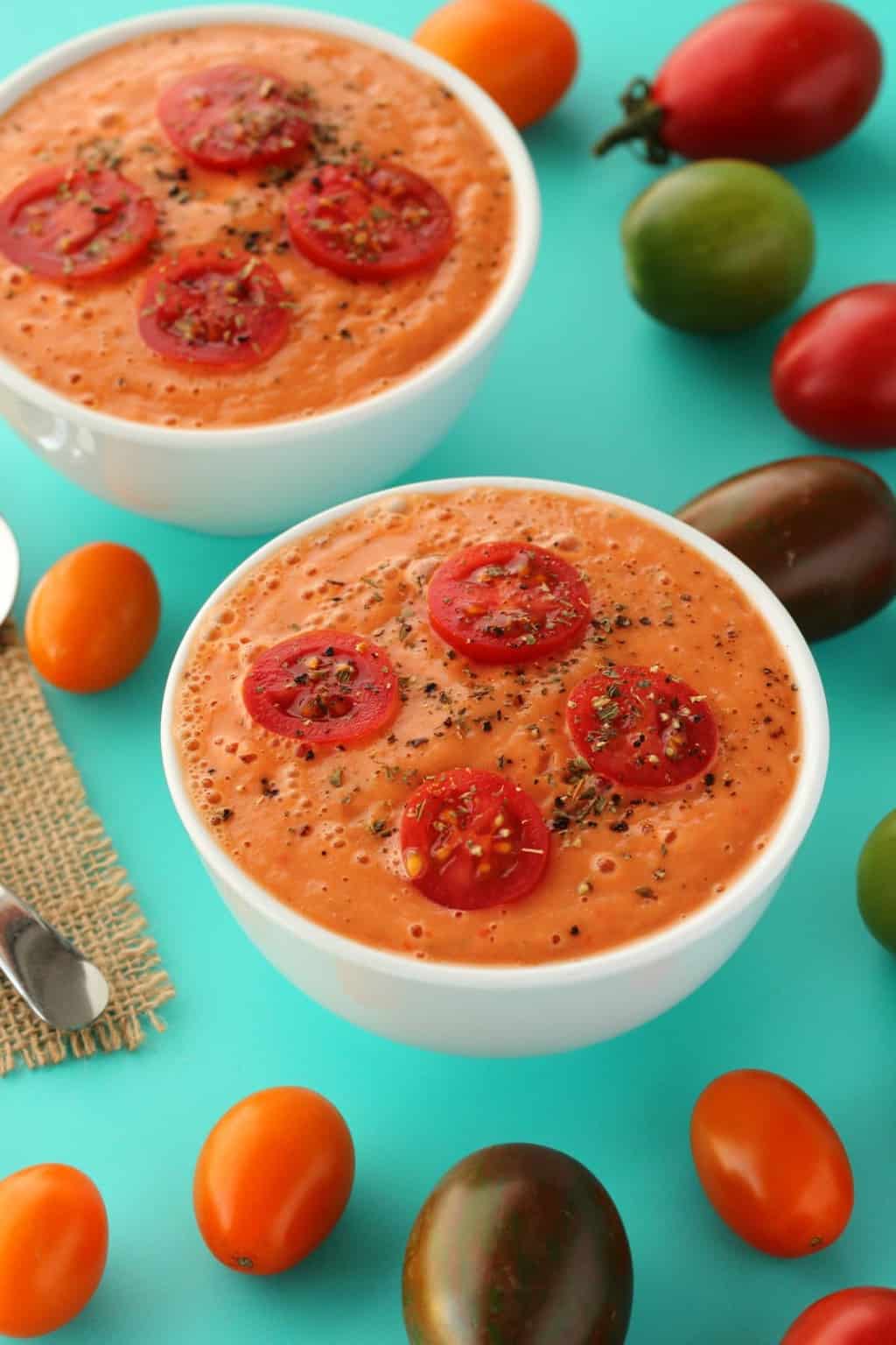 Raw tomato soup topped with sliced cherry tomatoes in white bowls. 