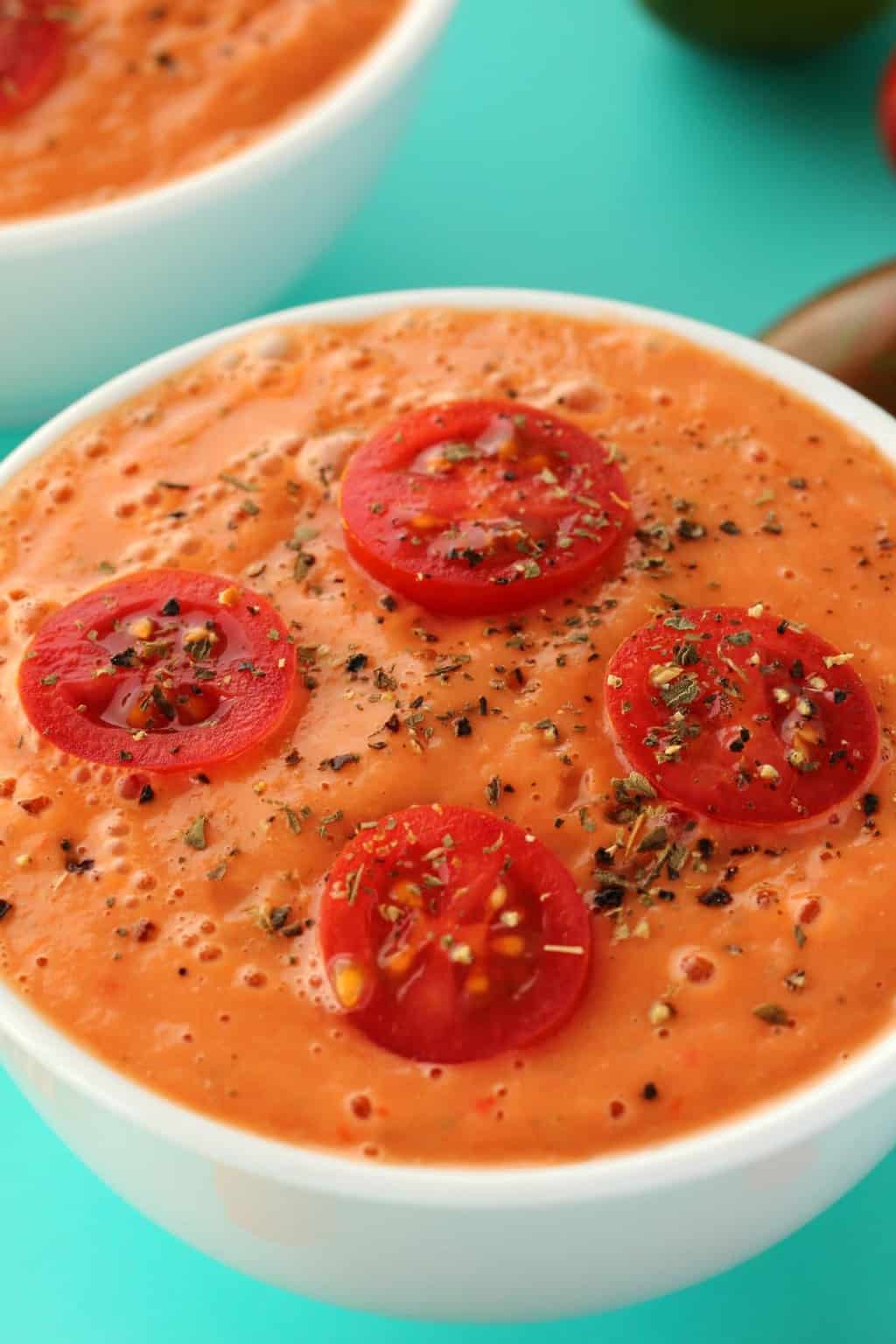 Raw tomato soup topped with sliced cherry tomatoes in a white bowl. 