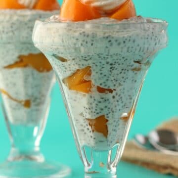 Chia pudding in dessert glasses topped with peaches and whipped cream.