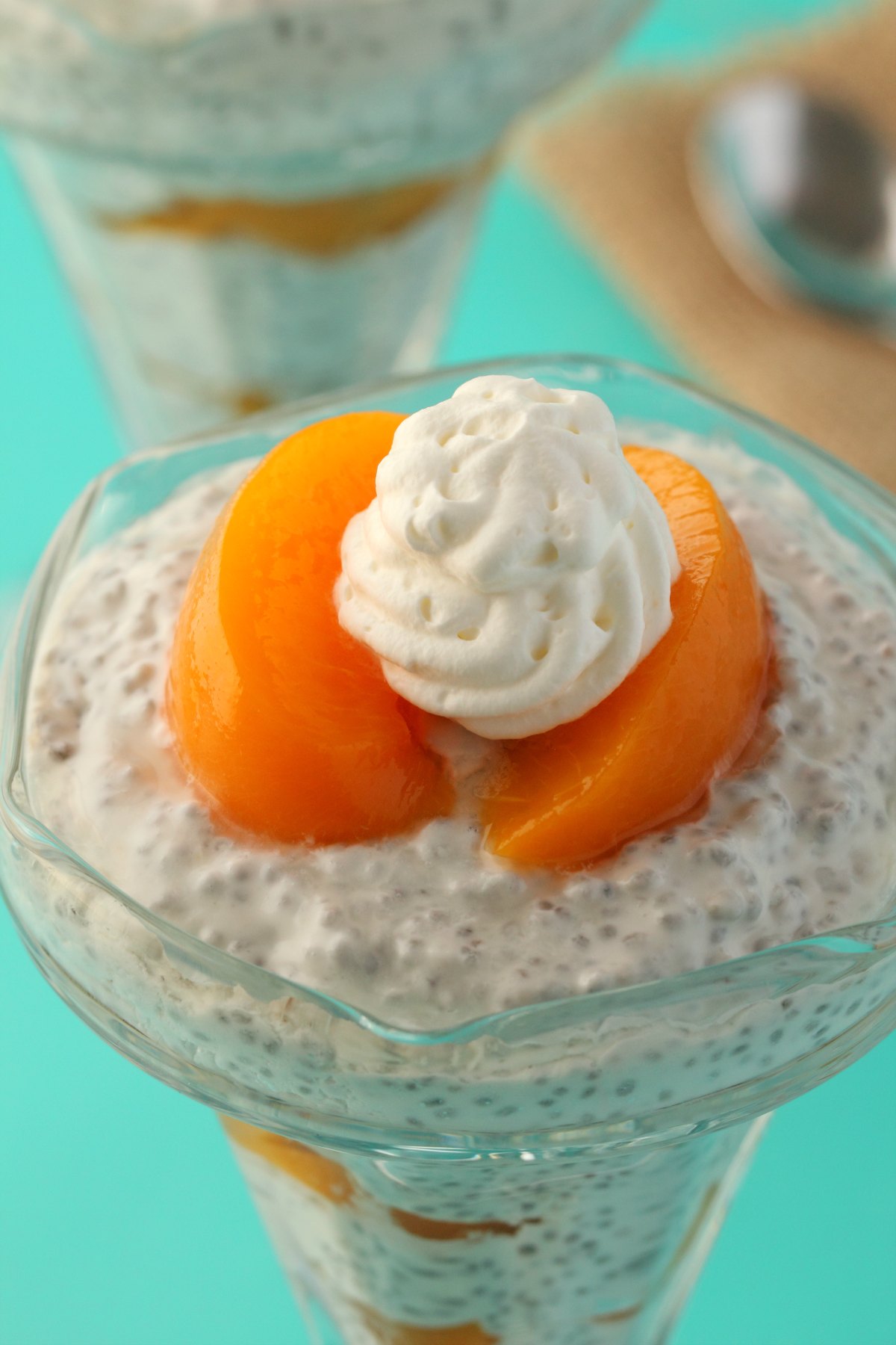 Chia pudding and peach slices layered in sundae glasses and topped with vegan whipped cream. 
