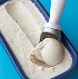 Vegan vanilla ice cream in a blue ceramic loaf pan with an ice cream scoop.