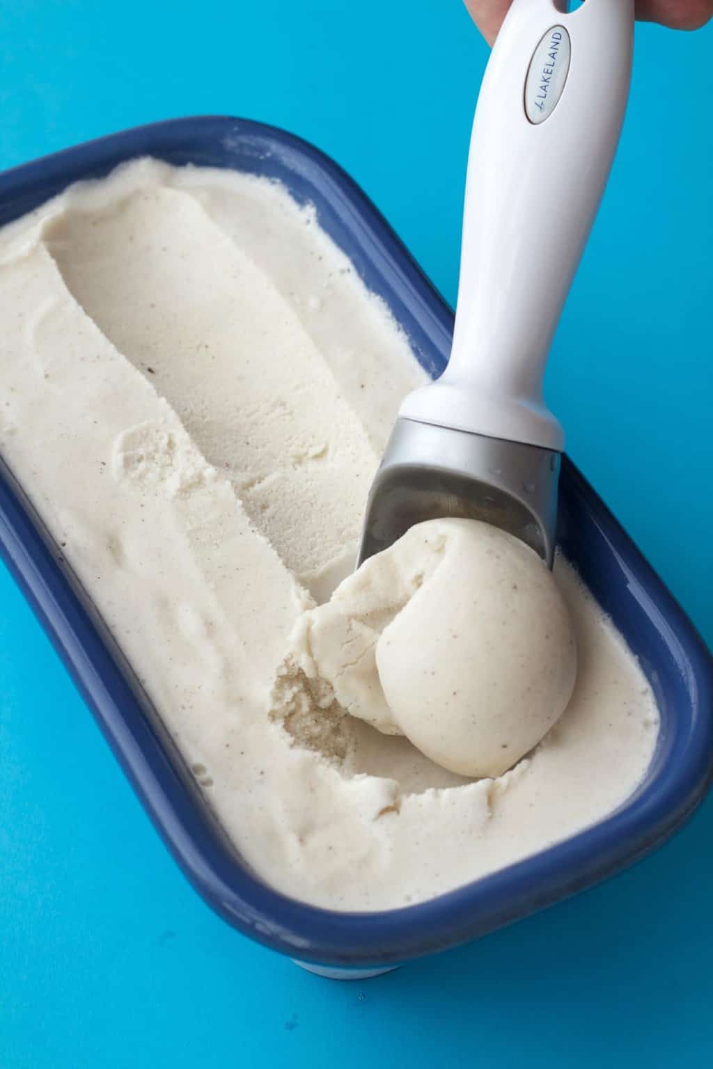 Vegan vanilla ice cream in a blue ceramic loaf pan with an ice cream scoop. 