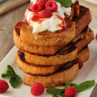 Vegan french toast topped with whipped cream and raspberries on a white plate.