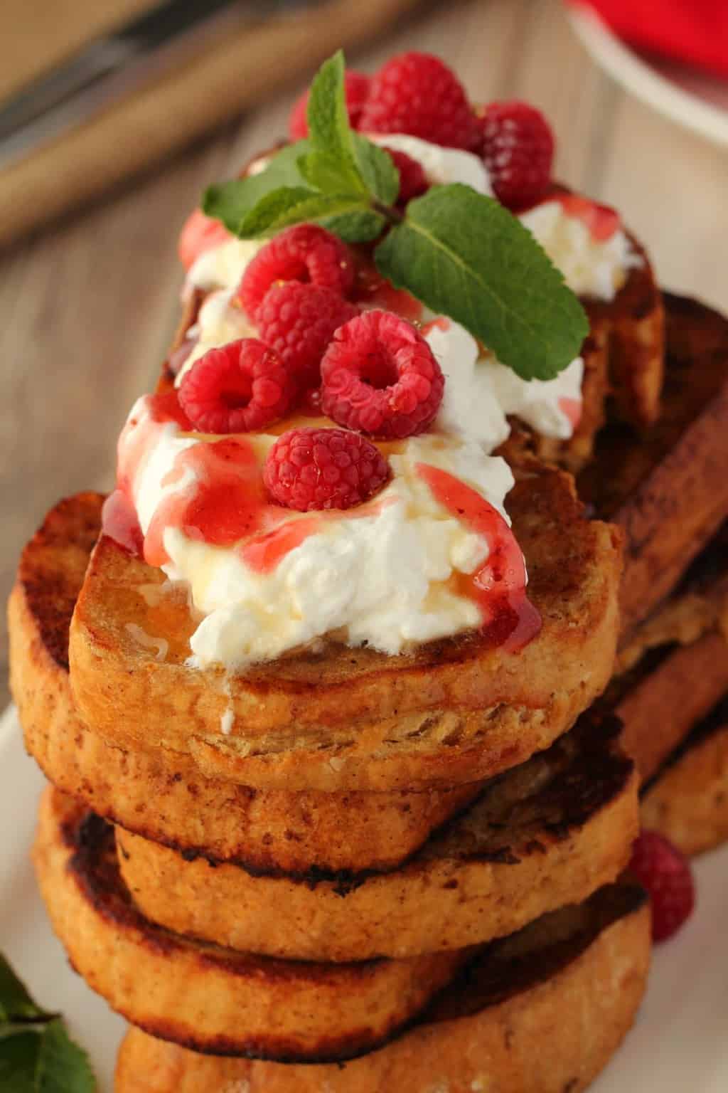 A stack of vegan french toast topped with vegan whipped cream and raspberries. 