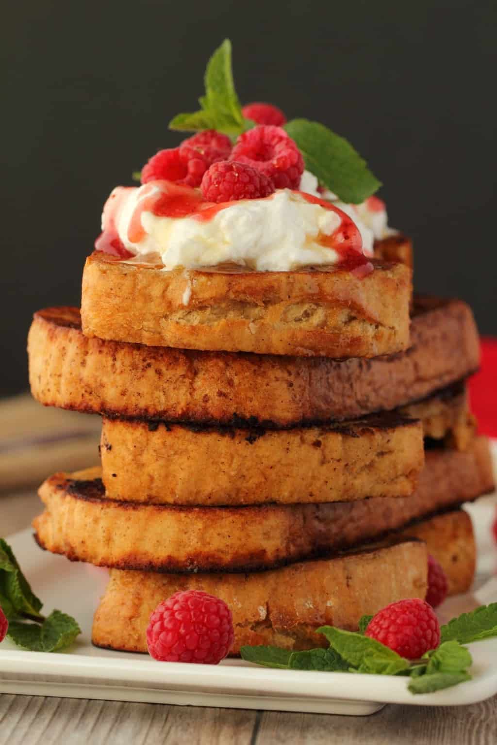 A stack of vegan french toast topped with strawberry jam, syrup and whipped cream, on a white plate.