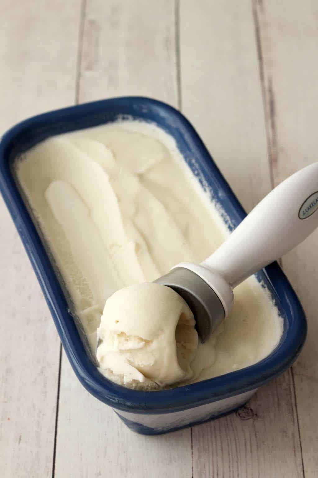 Vegan coconut ice cream in a blue ceramic dish with an ice cream scoop. 