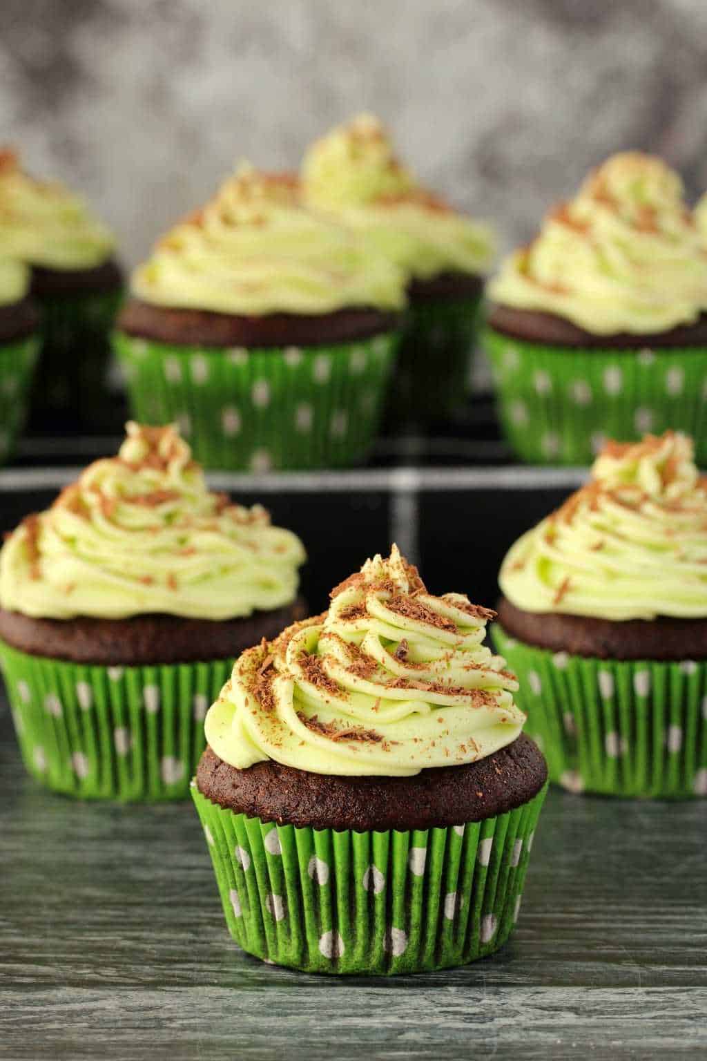 Vegan chocolate cupcakes topped with mint buttercream frosting against a dark background. 