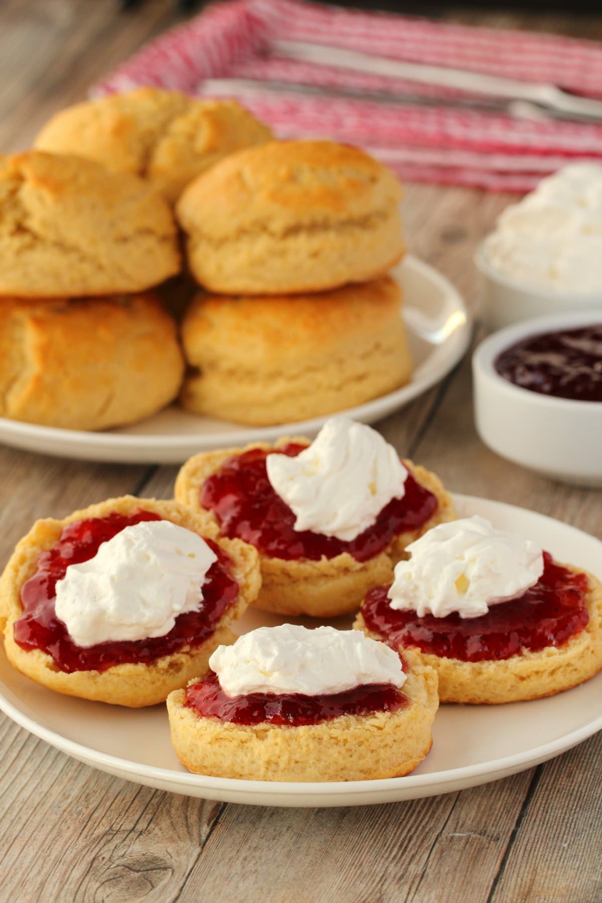 Vegan scones topped with jam and vegan whipped cream on a white plate. 