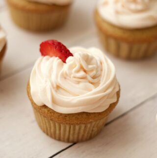 Vegan vanilla cupcakes topped with frosting and sliced strawberries.