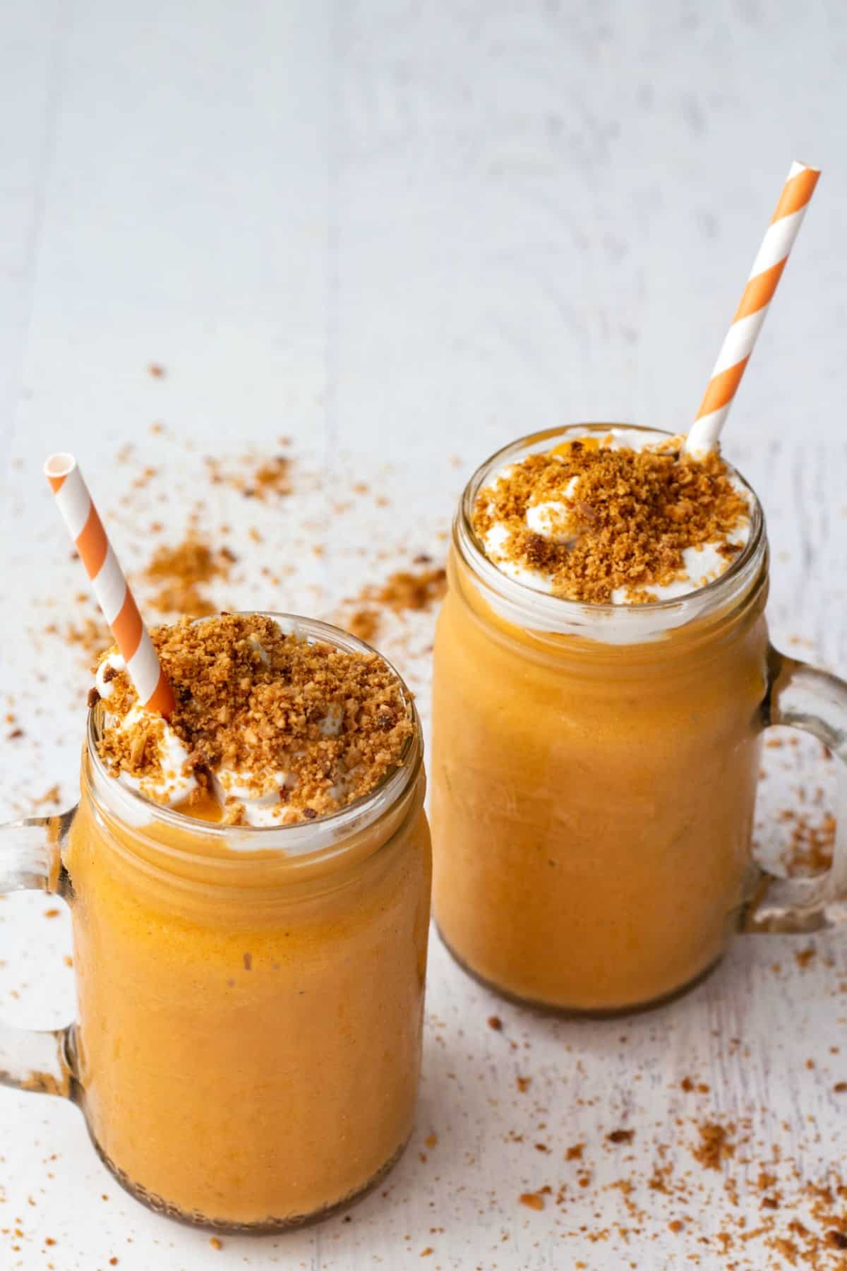 Smoothie with cream and toasted coconut in two glasses with orange and white striped straws. 