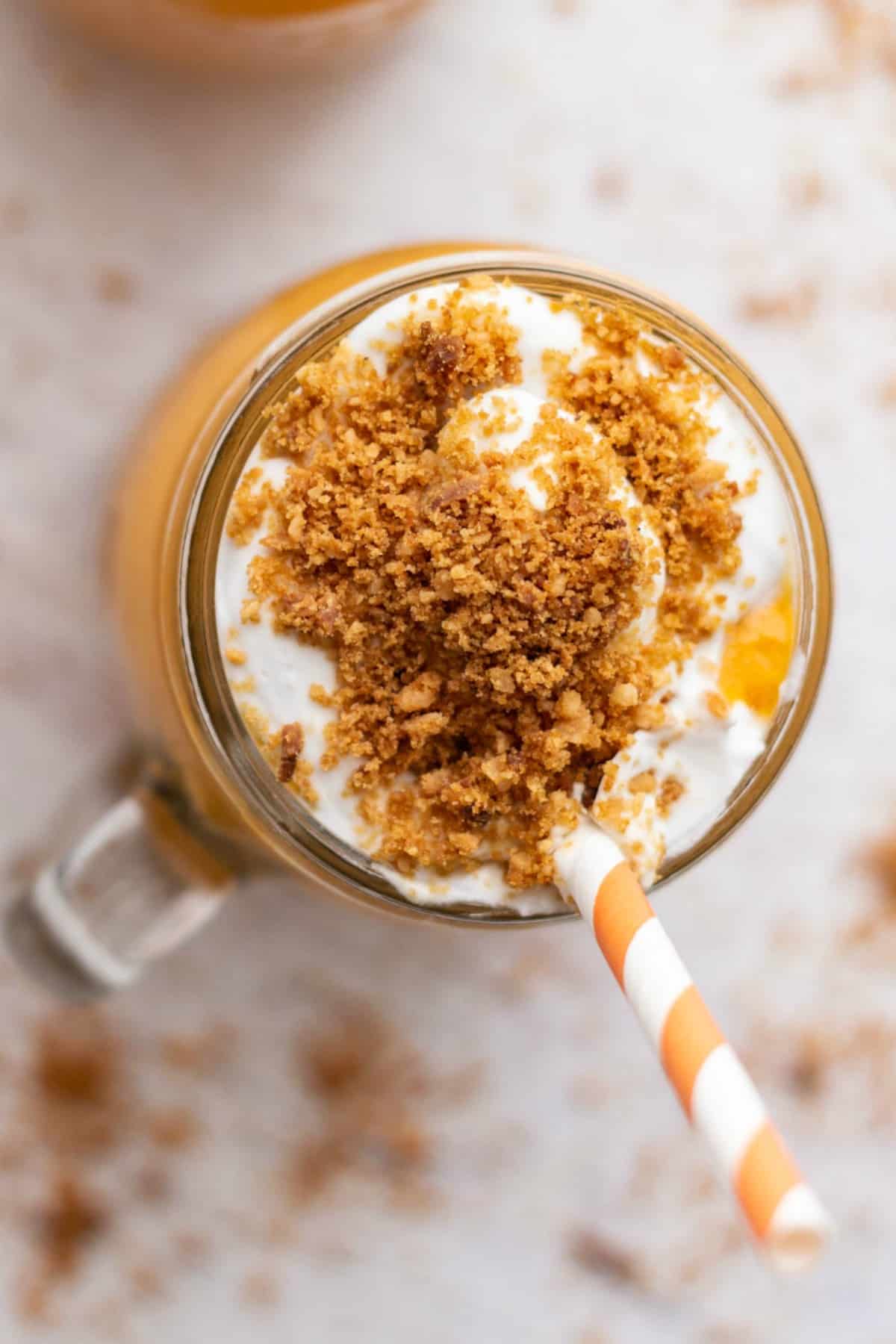 Carrot cake smoothie in a glass with an orange and white striped straw. 