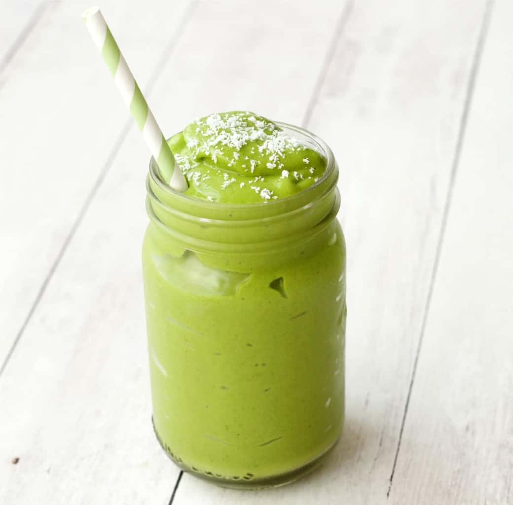 Matcha green tea smoothie topped with a sprinkle of dessicated coconut in a glass with a green and white striped straw. 