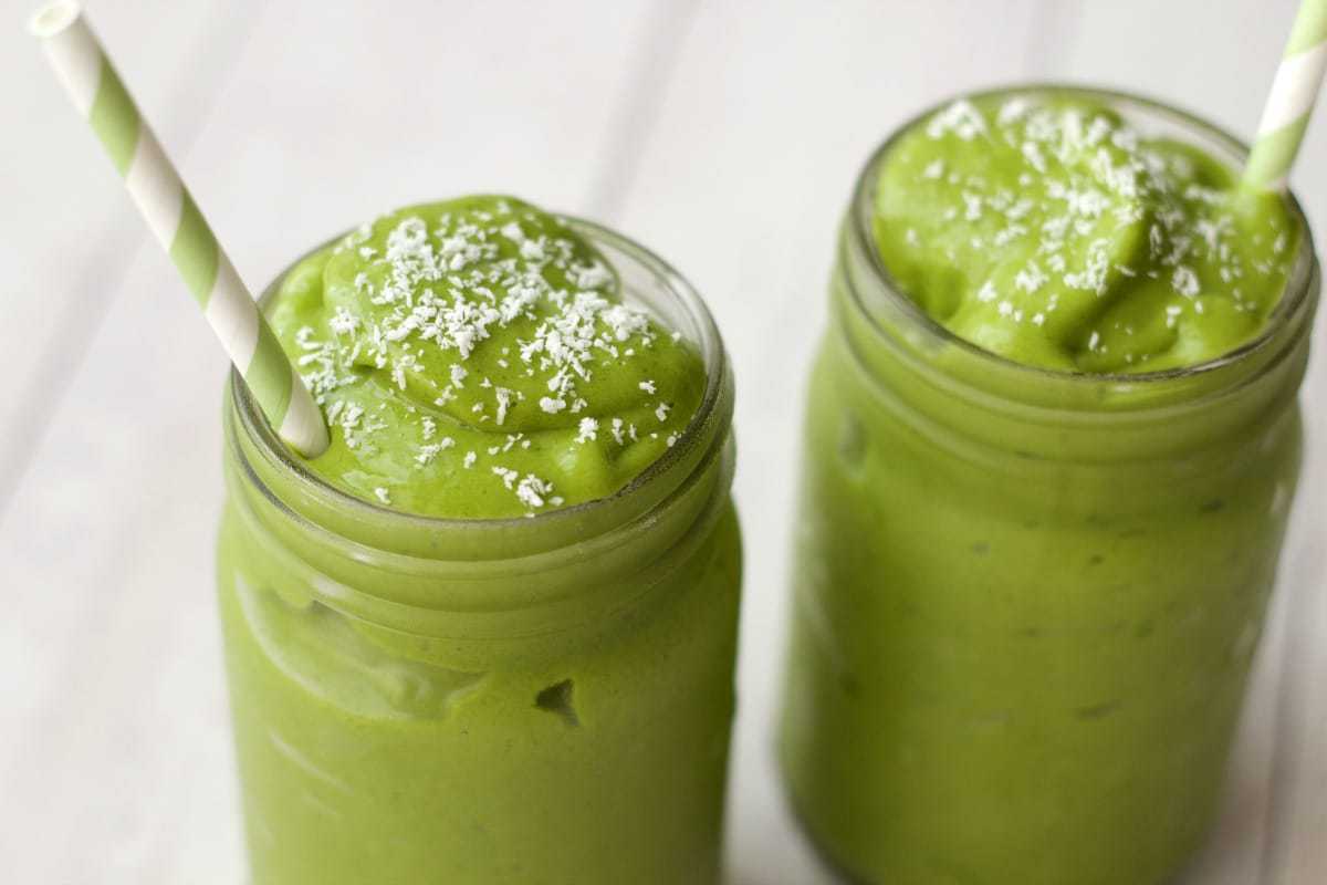 Matcha green tea smoothie topped with a sprinkle of dessicated coconut in glasses with green and white striped straws. 