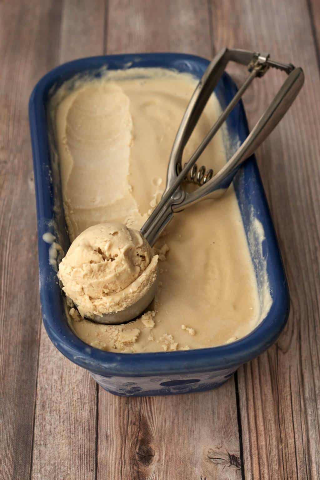 Salted caramel ice cream in a ceramic loaf pan with an ice cream scoop. 