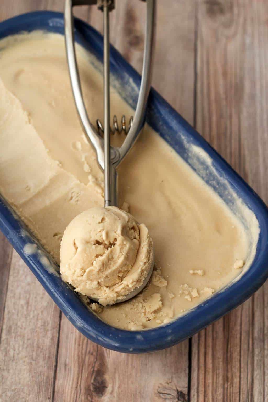 Salted caramel ice cream in a ceramic loaf pan with an ice cream scoop. 