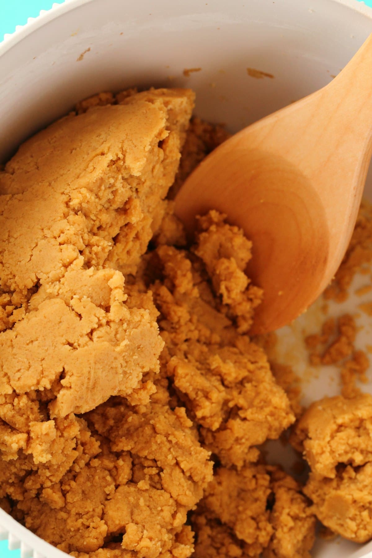 Cookie dough for vegan peanut butter cookies in a bowl with a wooden spoon. 