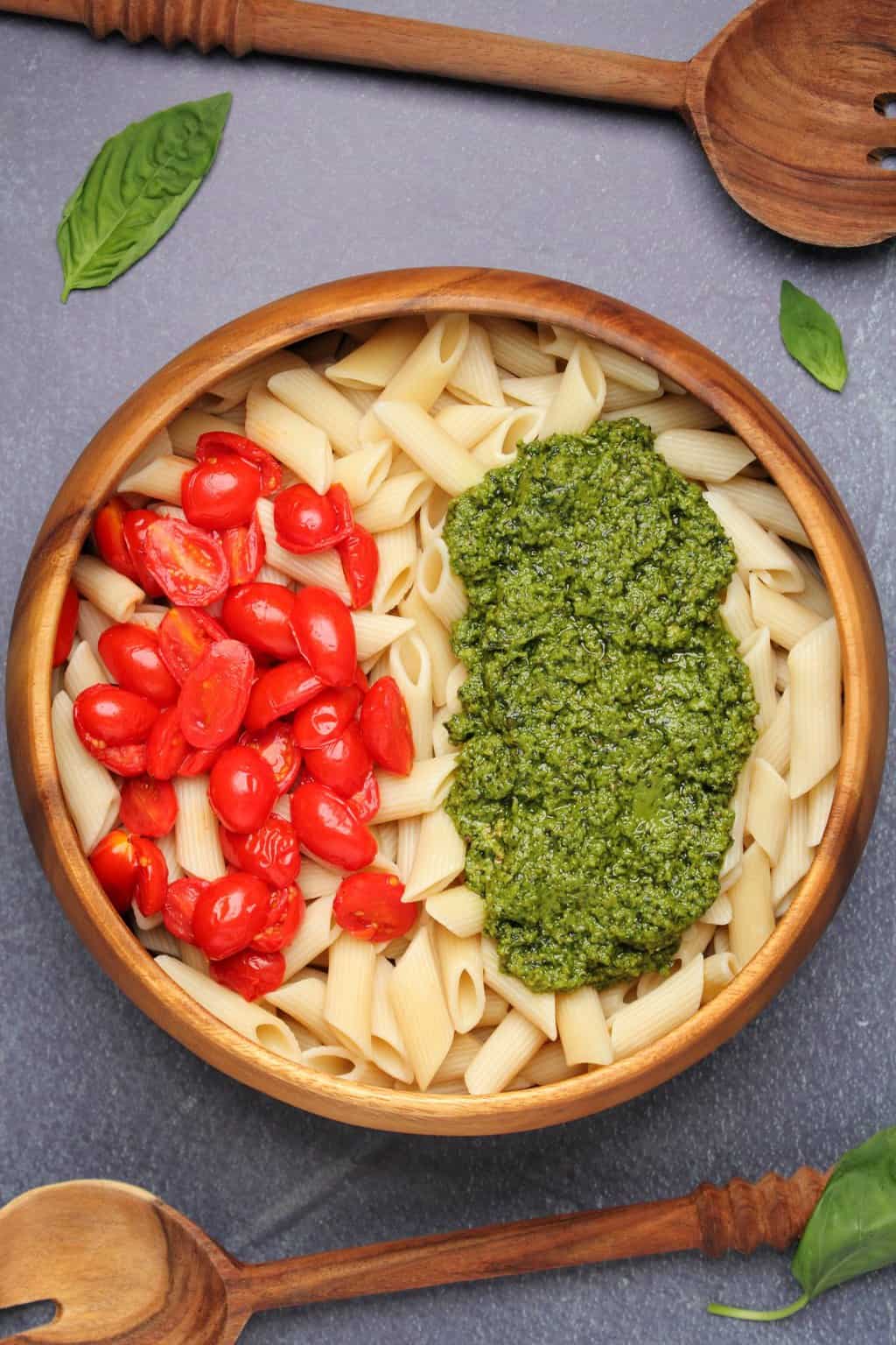 Penne pasta topped with vegan pesto and pan roasted cherry tomatoes in a wooden salad bowl. 