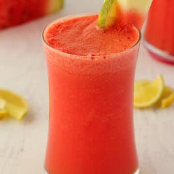 Watermelon smoothie in a glass with a green and white striped straw.