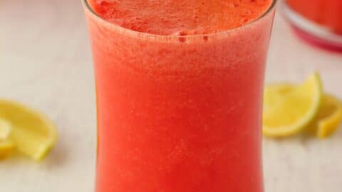 Watermelon smoothie in a glass with a green and white striped straw.