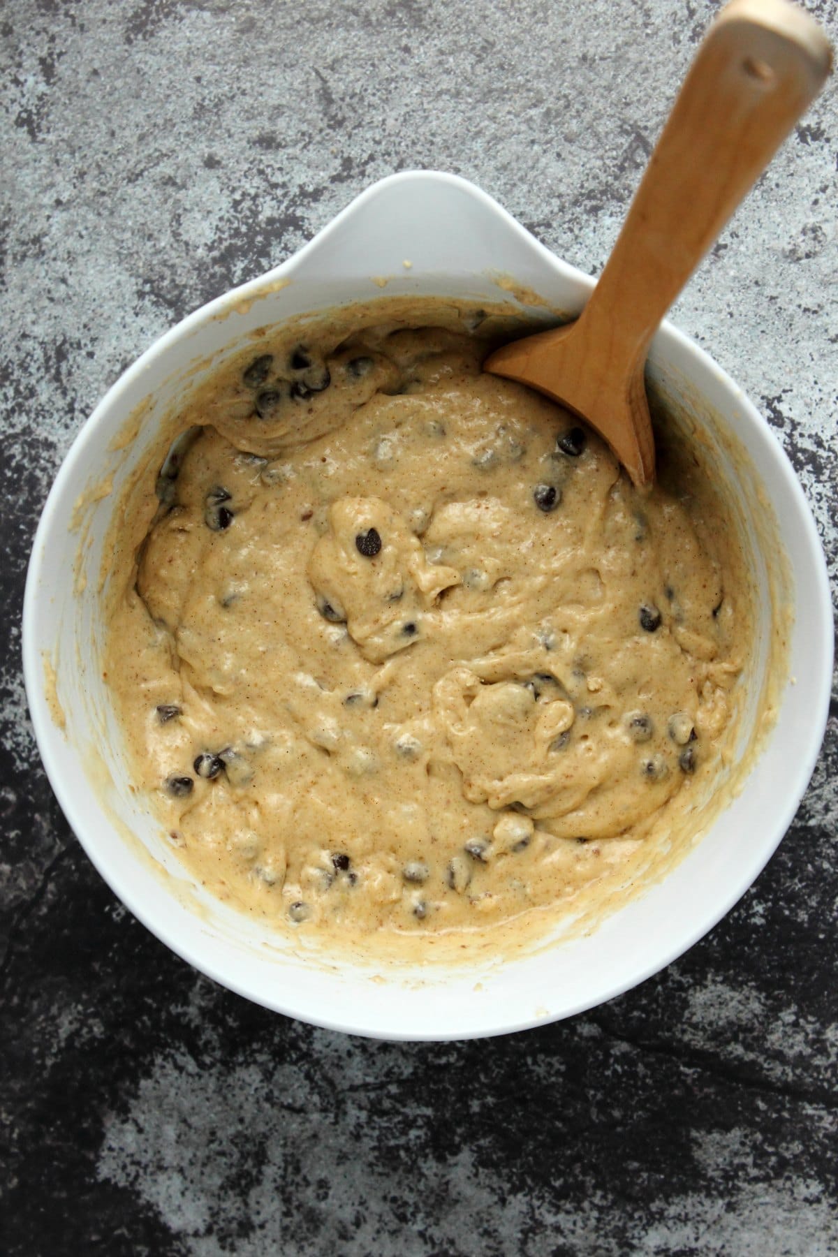Batter for chocolate chip banana bread in a mixing bowl with a wooden spoon.