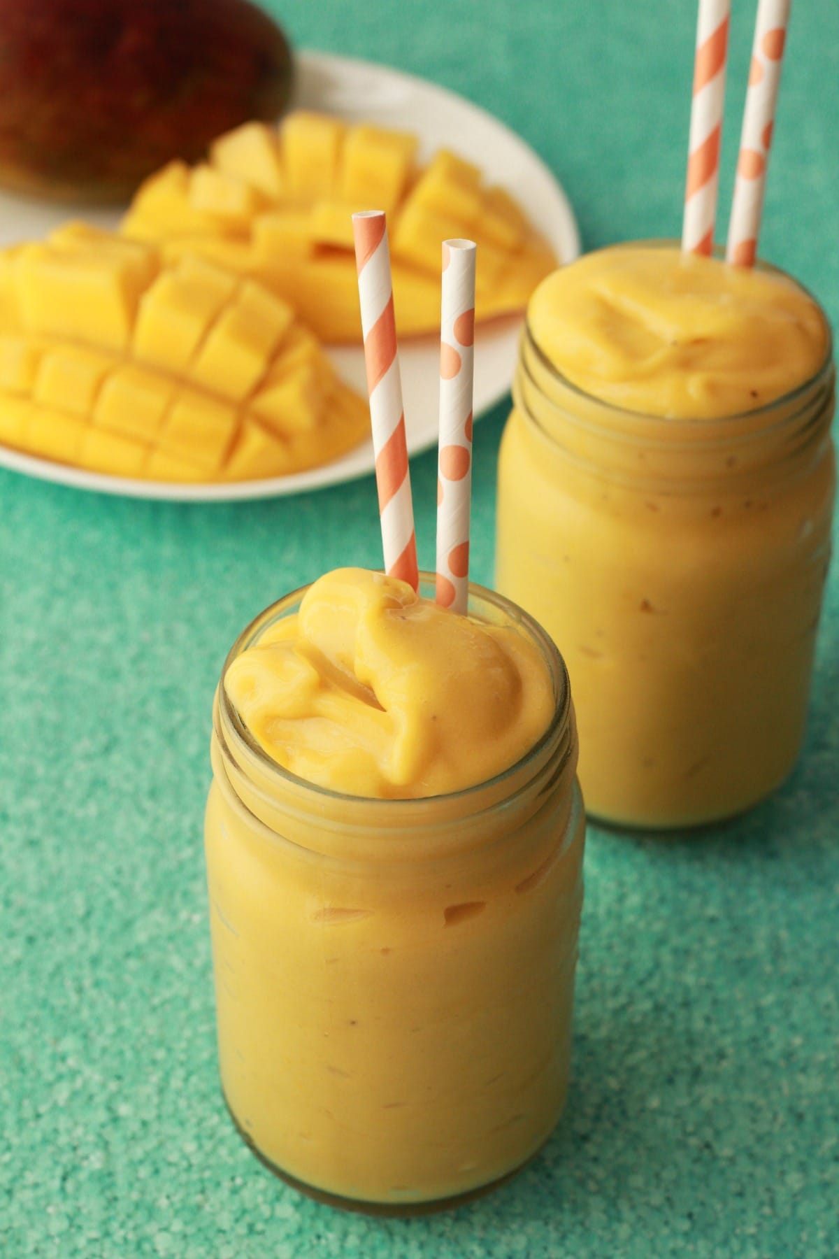 Mango smoothie in glasses with orange and white straws. 