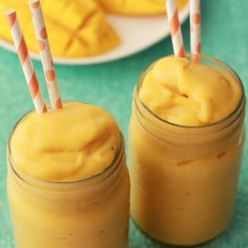Mango smoothie in glasses with orange and white striped straws.