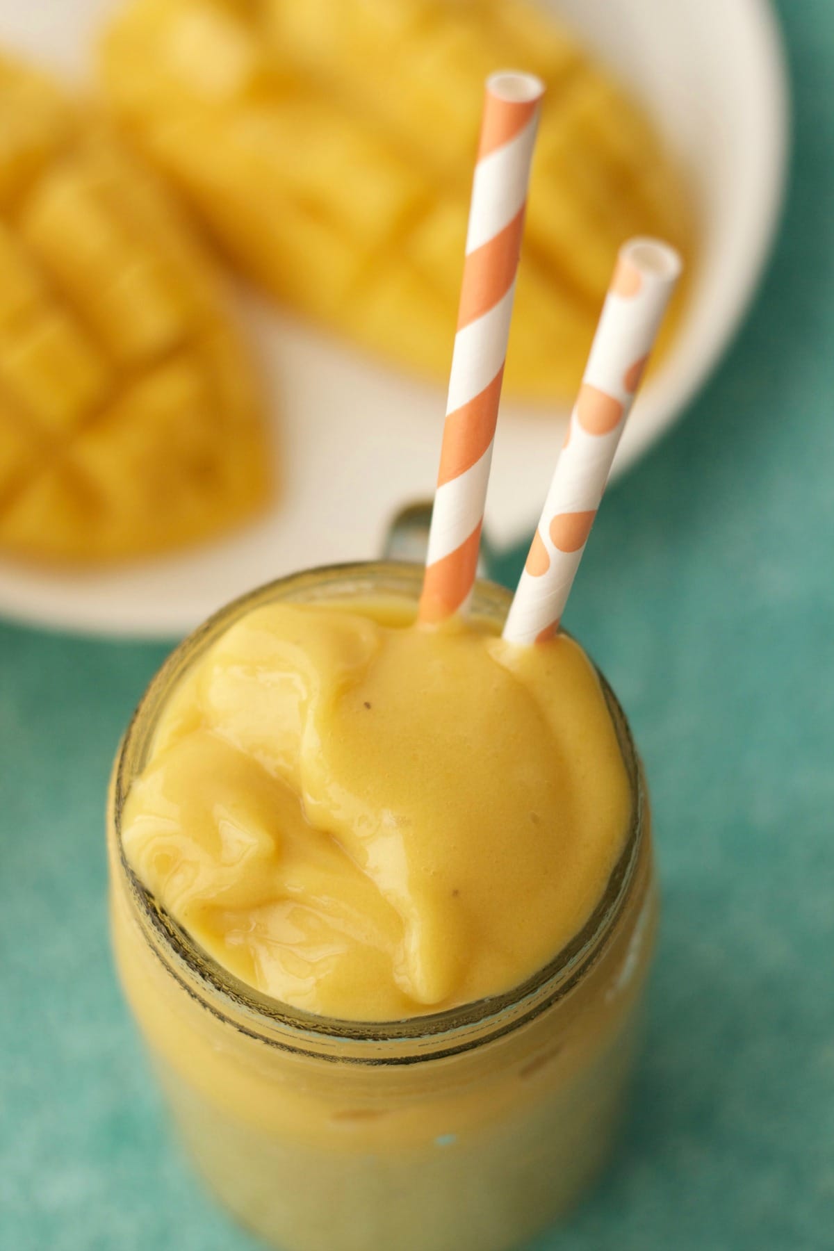 Mango smoothie in a glass with orange and white straws. 