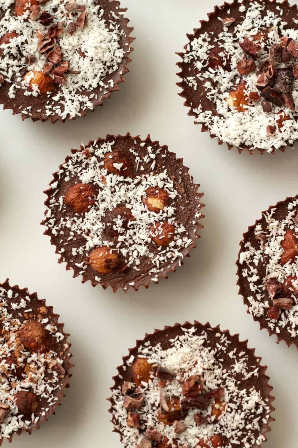 Raw chocolate cups topped with shredded coconut and cacao nibs on a white plate. 