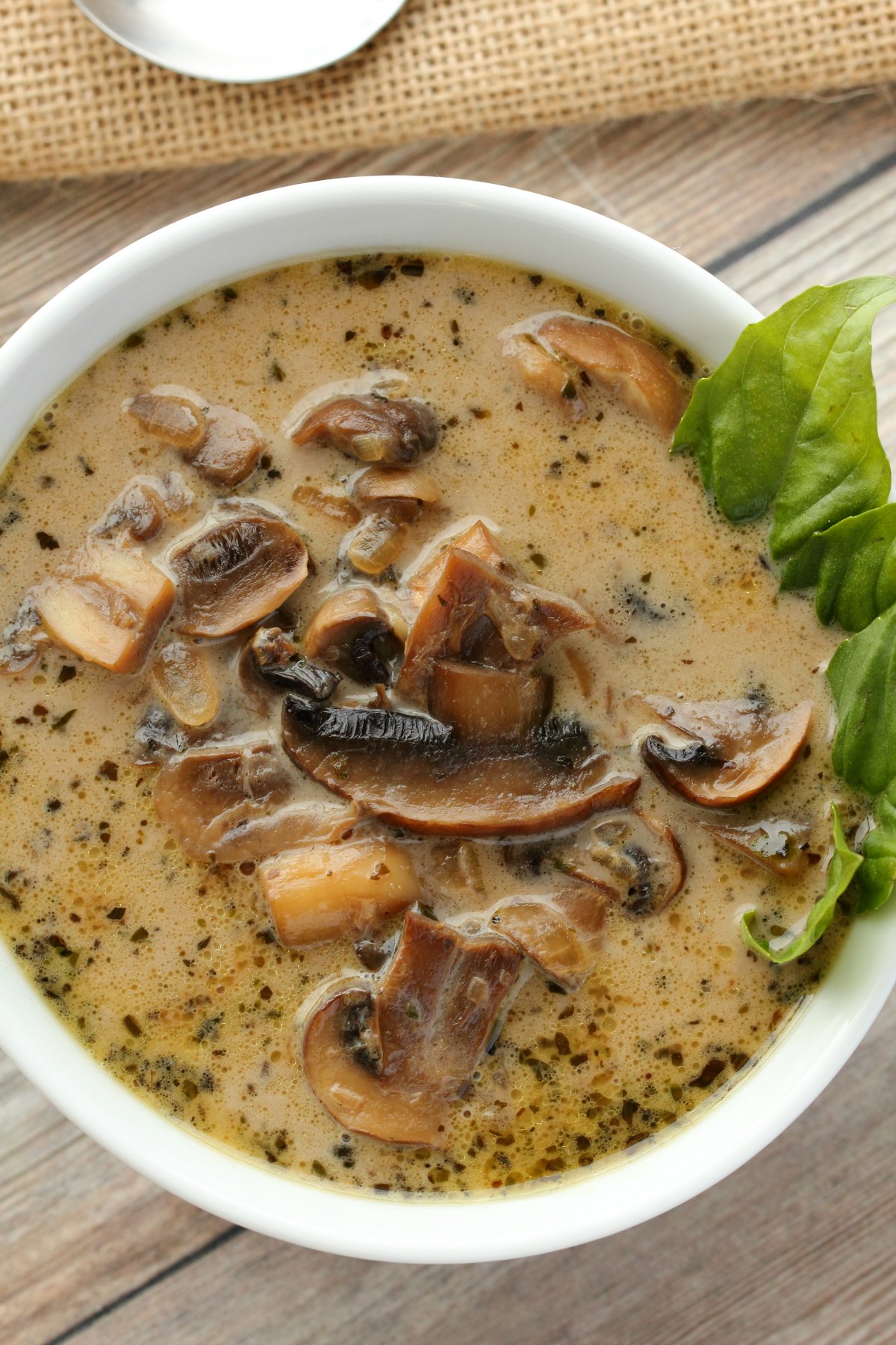 Vegan mushroom soup in a white bowl with fresh basil leaves. 