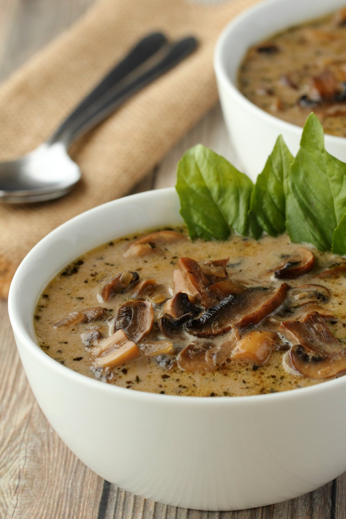 Vegan mushroom soup in a white bowl with fresh basil leaves. 