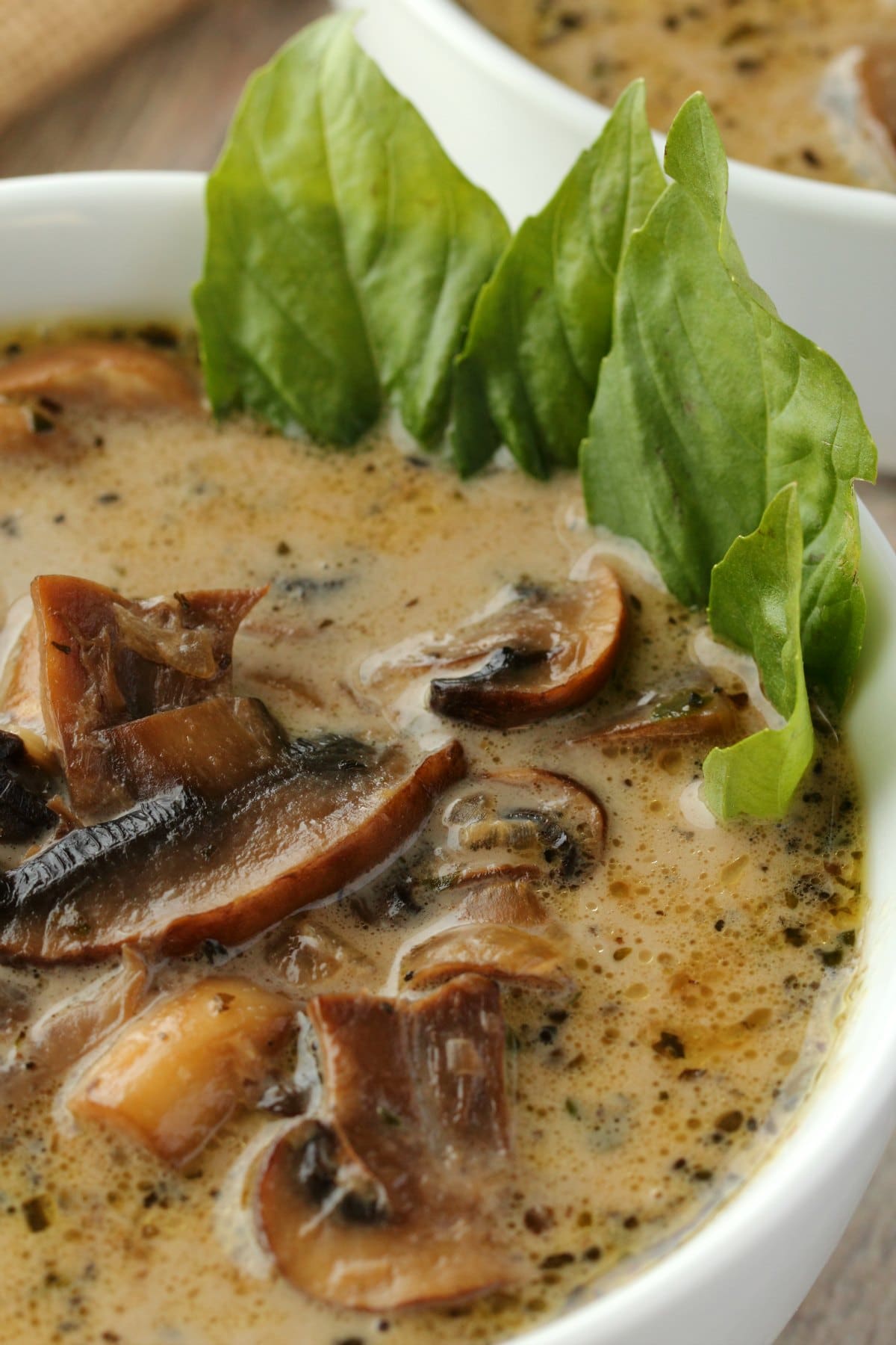 Vegan cream of mushroom soup in a white bowl with fresh basil. 