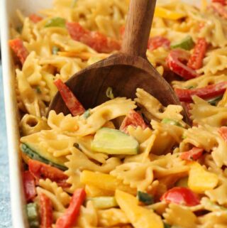 Vegan pasta salad in a white dish with a wooden serving spoon.