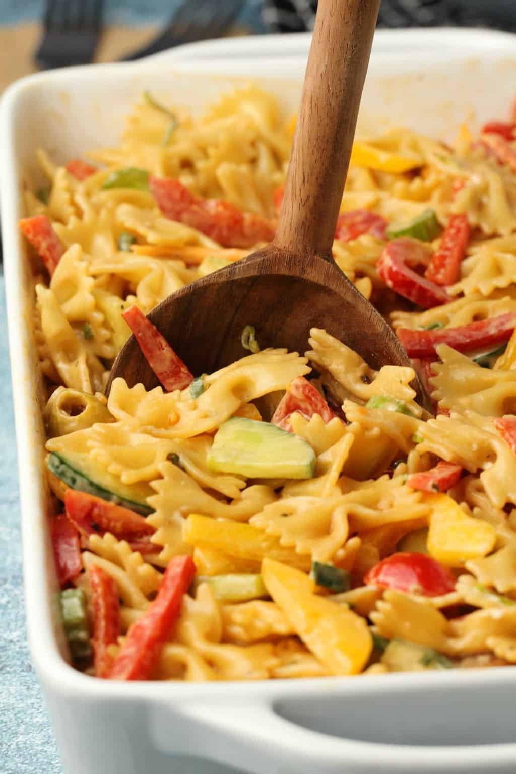 Vegan pasta salad in a rectangular white dish with a wooden salad spoon. 