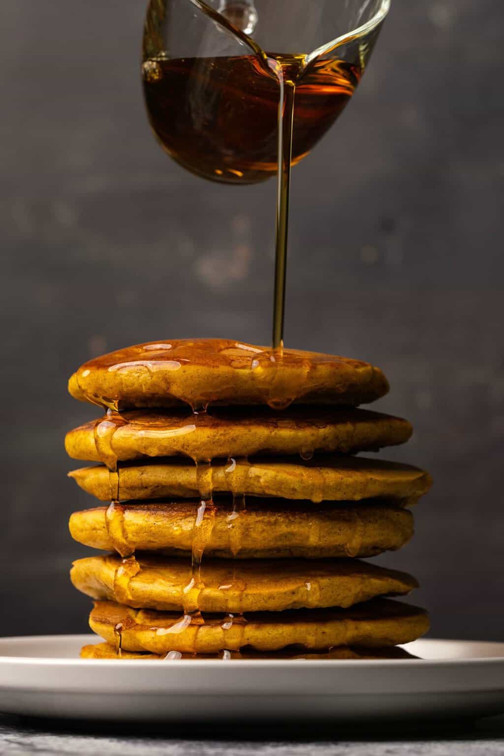 Syrup pouring onto a stack of vegan pumpkin pancakes.